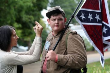 woman flipping her middle fingers in front of a young man holding a confederate flag