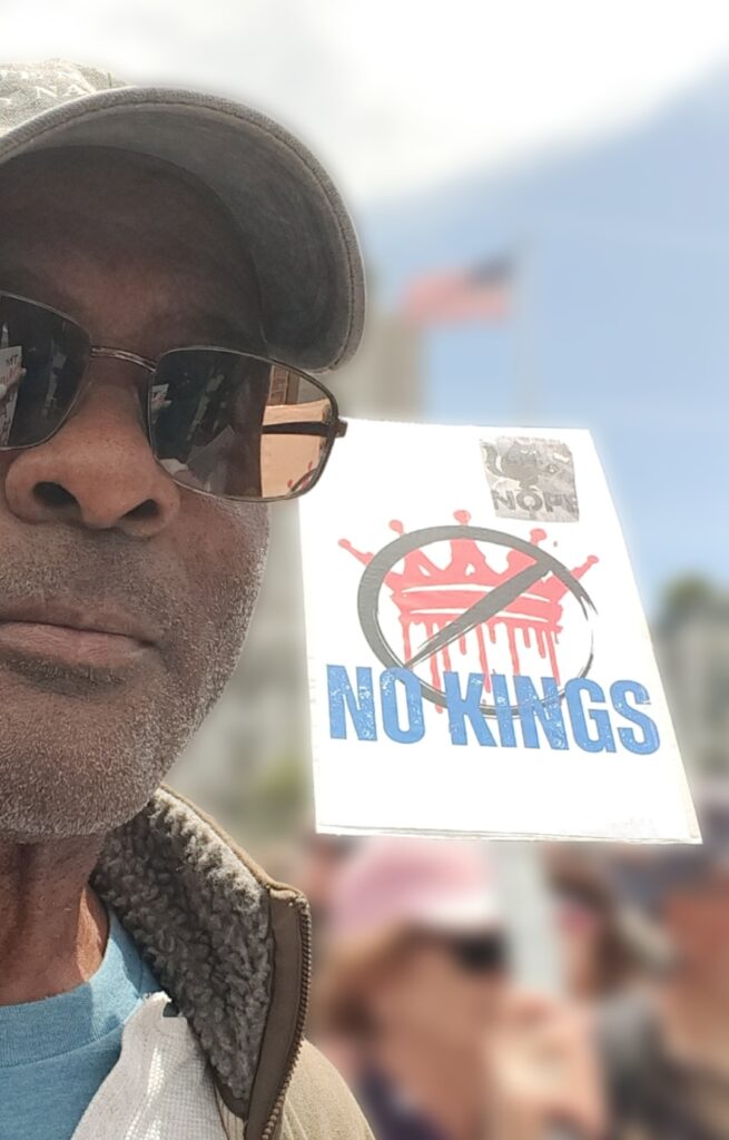 The author standing next to a "No Kings" sign at the No Kings protest rally in San Francisco's Civic Center.