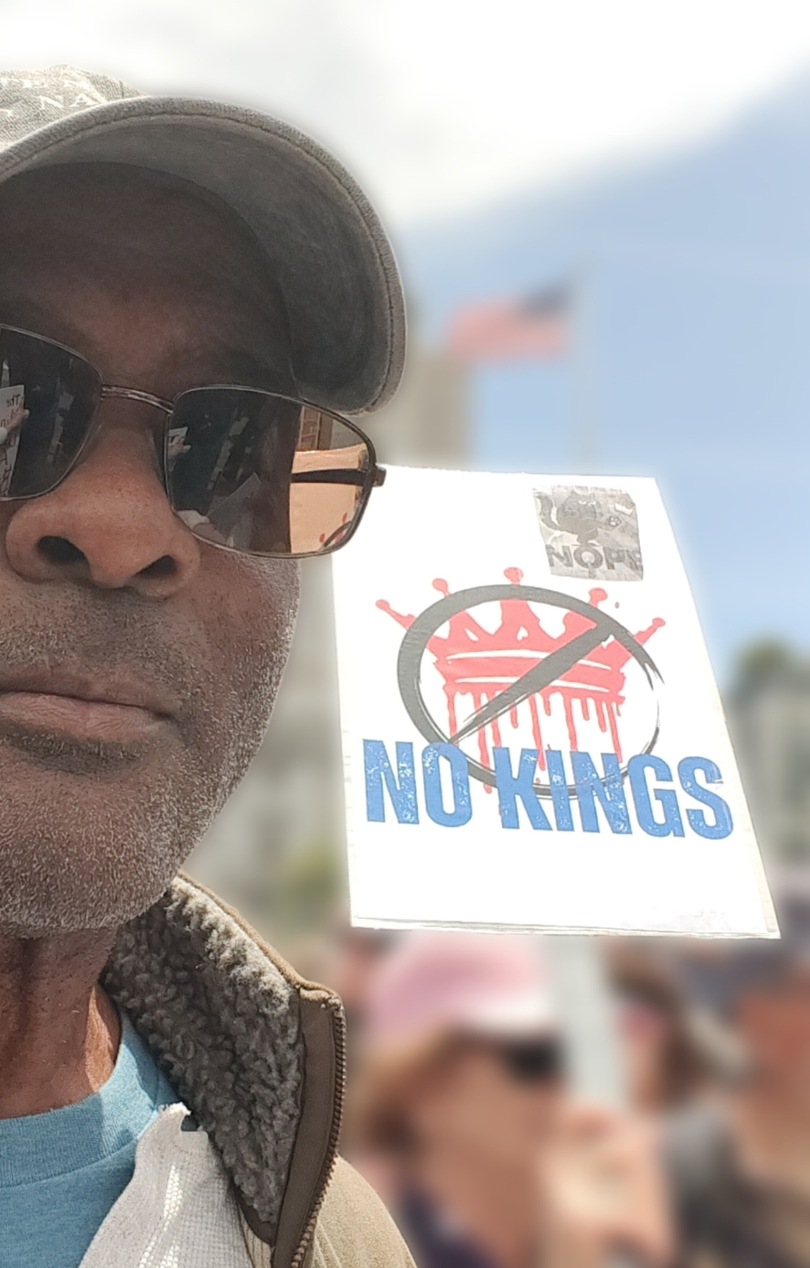 The author standing next to a "No Kings" sign at the No Kings protest rally in San Francisco's Civic Center.